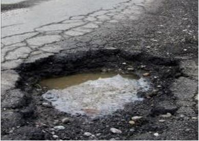 Very large and deep pothole full of water, in a road