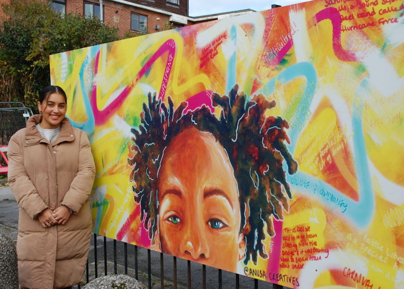 Artist Gemma Anusa standing next to her mural
