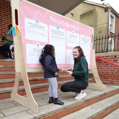 Picture shows a woman and a child interacting with the Ideas board for Oxford Road.