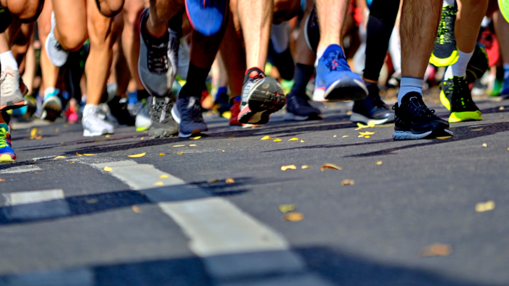 The picture shows a a large group of marathon runners feet as they are running on a tarmac road.