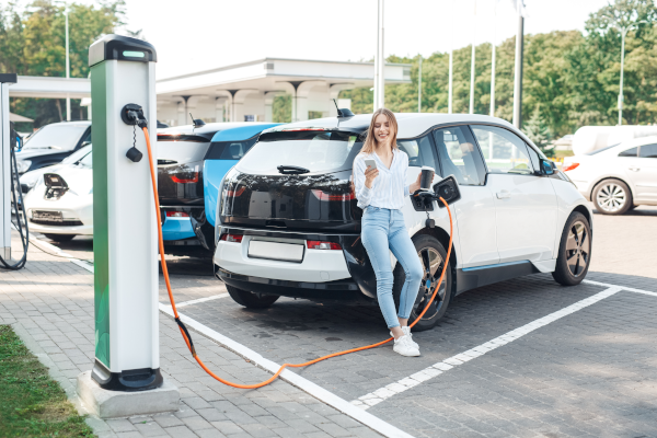 Woman leaning on electric car as it charges.