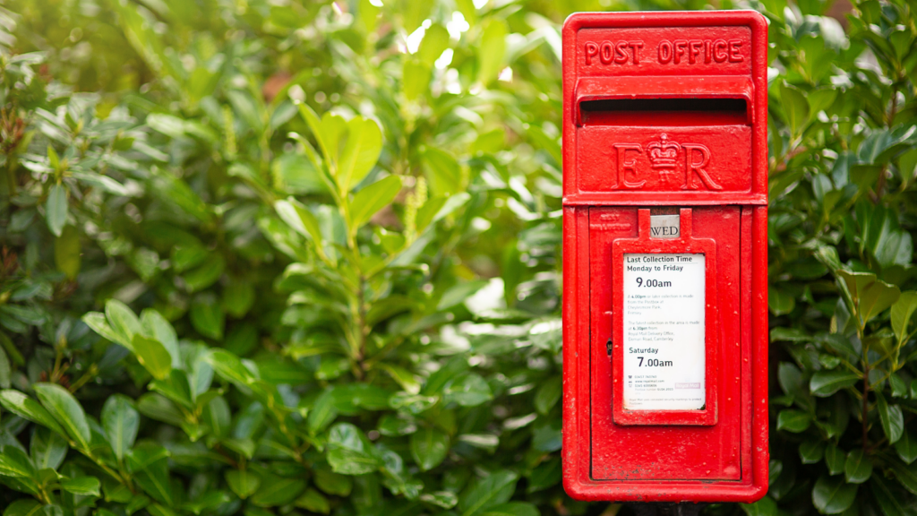 Royal Mail postbox in front of a green bush.