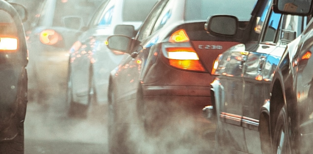 Two lanes of cars closely packed, showing clouds of exhaust smoke.