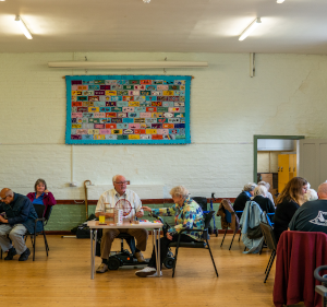 Older people sat at tables in a large hall playing games.