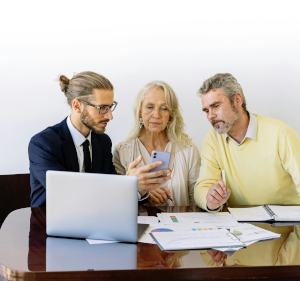 A man sat in front of a laptop talking to another man and a woman.