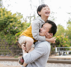 Man smiling as he lifts a laughing boy with Down's syndrome up.