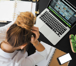 Overhead view of a woman with her head in her hands working on her laptop.