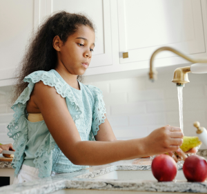 Young girl washing fruit at a kitchen sink.