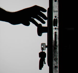 Black and white image of a hand reaching to a door handle, with keys hanging from the door.