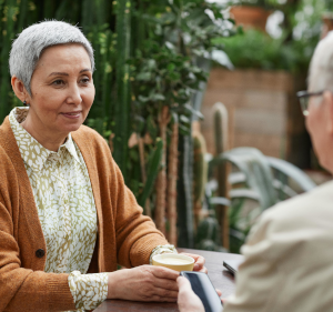 Woman sat outside at a table talking to a man.