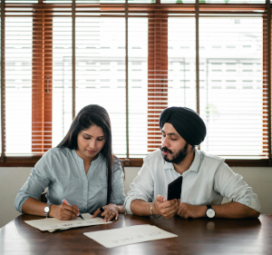 Man and woman sat at a table. The woman is writing on a piece of paper.