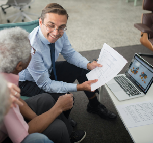 Man sat alongside woman, showing her a document.