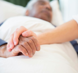 People holding hands on a sheet whilst one of them is ill in bed.