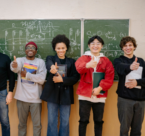 Four older children or young adults standing in front of a blackboard with their thumbs up.