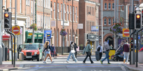  Four people in dark clothing walking across a zebra crossing (crosswalk) on a street, recreating the famous Abbey Road album cover pose by The Beatles.