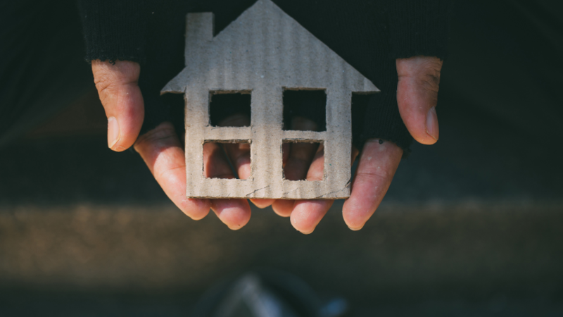 Hands in fingerless gloves holding a cardboard cutout of a house.