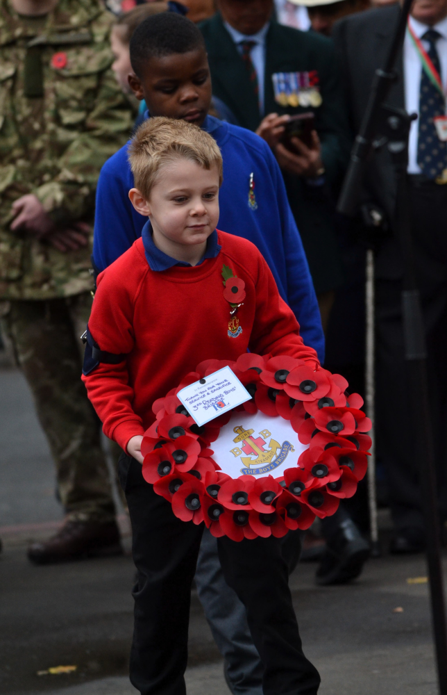 Multiple poppy wreaths laid at the base of Reading and Berkshire war memorial, with inscription visible honouring men who gave their lives for King and Country