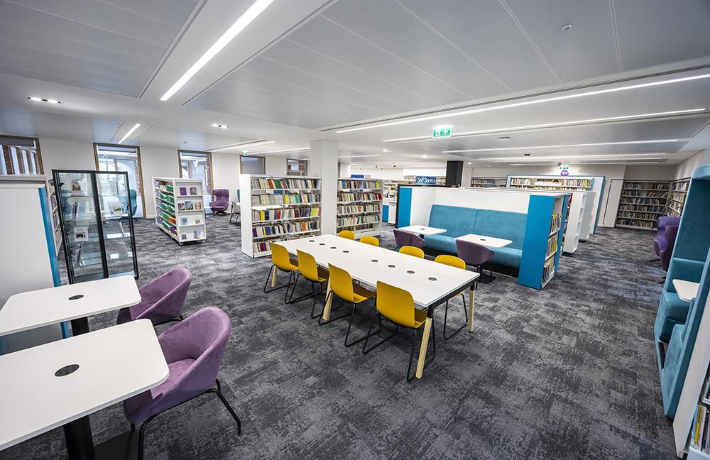 Modern Central Library reading area with bookshelves, study tables, booth seating, and comfortable chairs in a bright, quiet space.