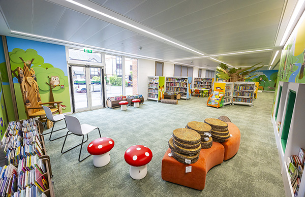 Spacious children's library featuring woodland-themed décor, book displays, mushroom stools, and flexible seating for reading and activities.