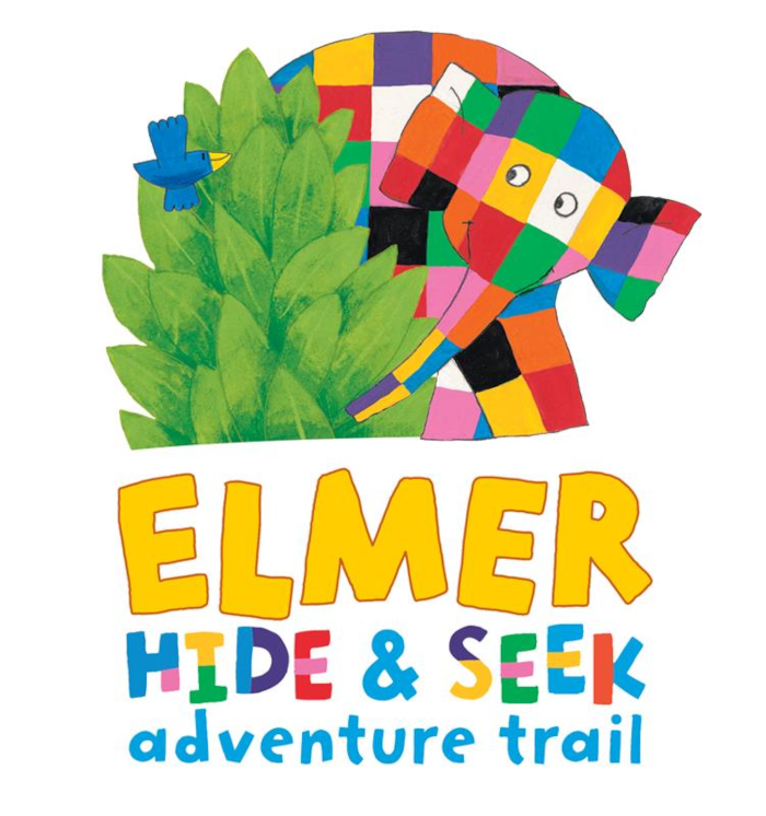 Illustrated poster for Elmer Hide & Seek Adventure Trail. Elmer, the patchwork elephant made of brightly coloured squares, peeks out from behind a large green bush while a small blue bird flies nearby. Below the illustration, the title reads “ELMER” in large yellow letters, followed by “HIDE & SEEK” in colourful letters and “adventure trail” in blue text on a light grey background.